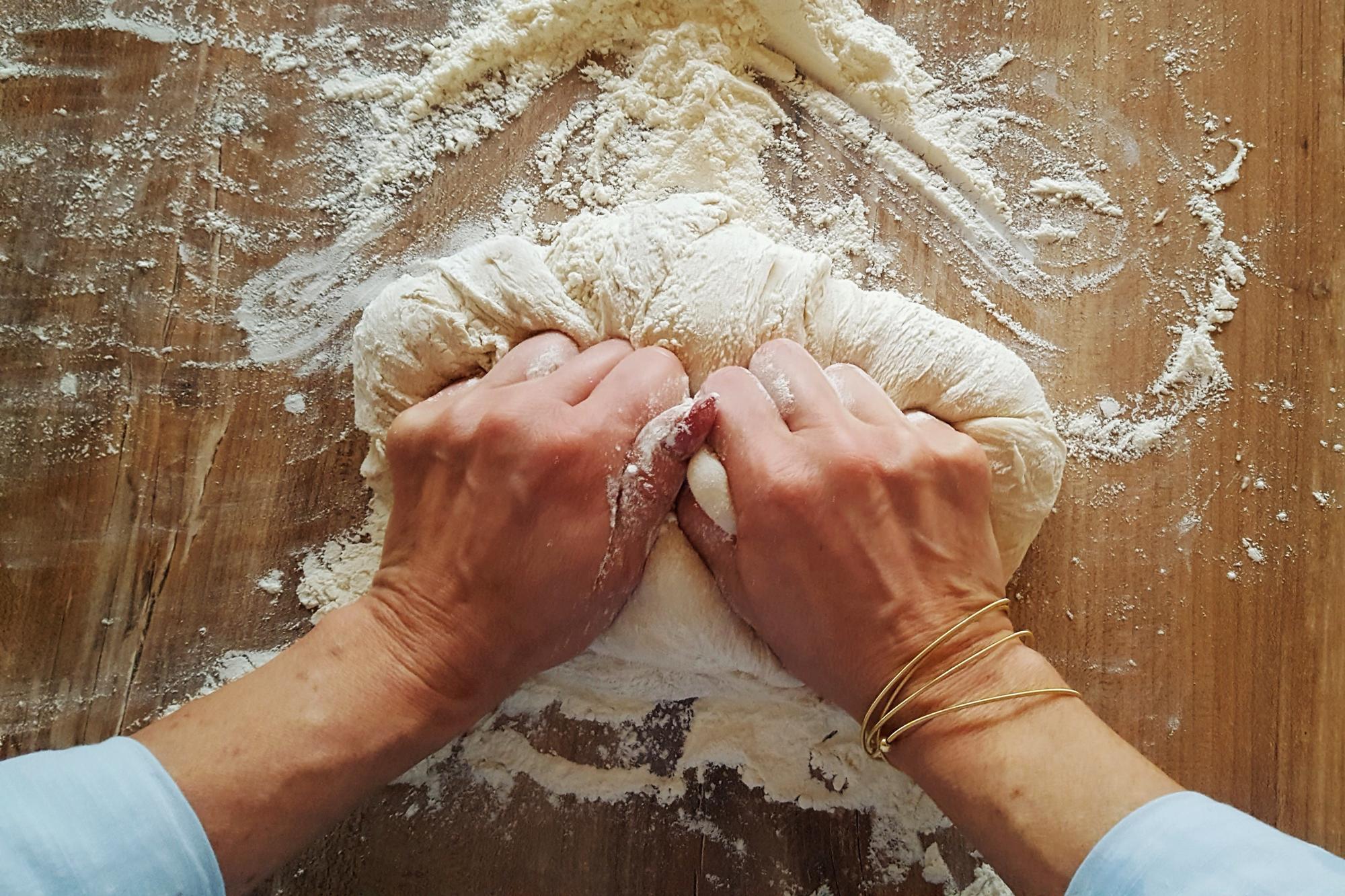 Hands kneading dough on floured board